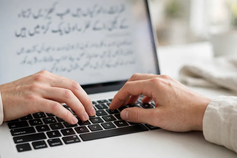 Hands in correct touch typing position on a laptop keyboard with Urdu text on screen