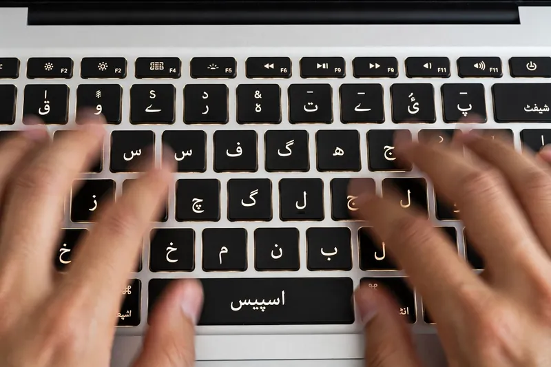 Hands typing fast on laptop keyboard with Urdu script key labels